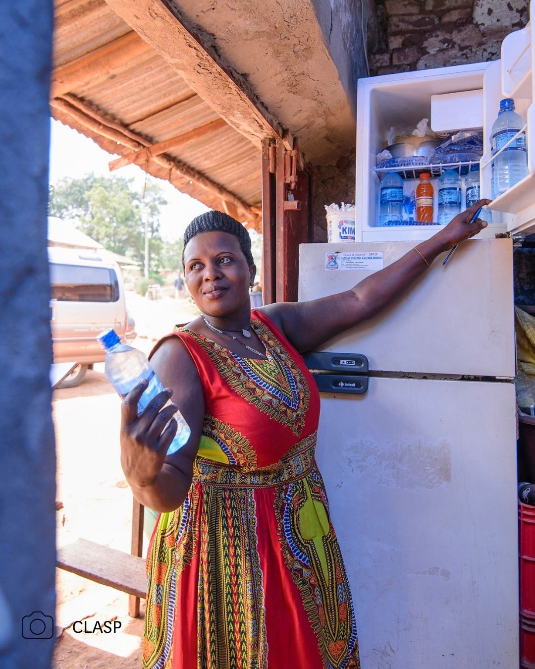 A woman in a vibrant dress opening a refrigerator, holding a water bottle.
